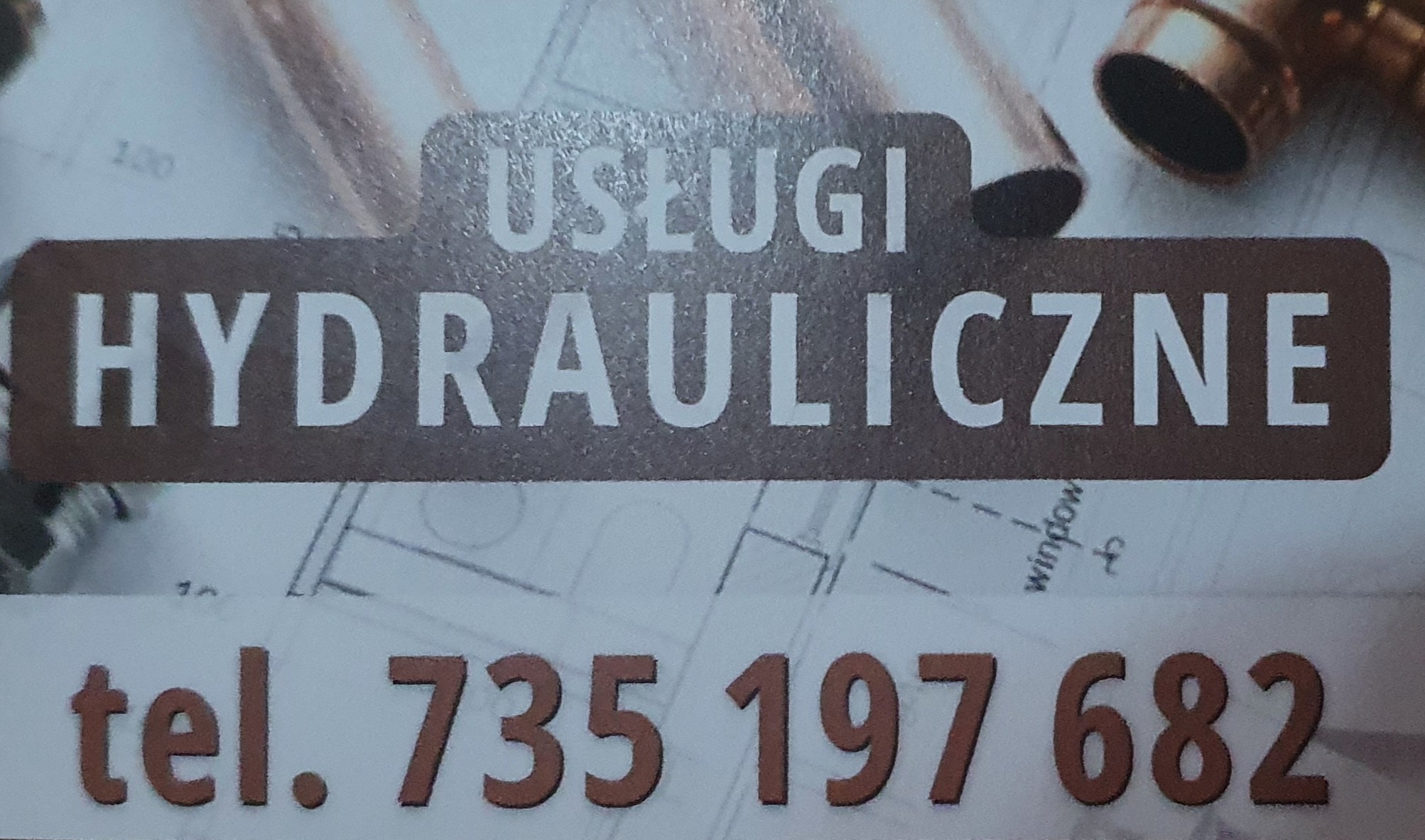 Wizytówka z napisem 'Usługi Hydrauliczne' i numerem telefonu 735 197 682, leżąca na tle planu instalacji i elementów rur miedzianych.