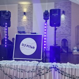 DJ PiTeR - Scena z nagłośnieniem, oświetleniem i stanowiskiem DJ-a z logo DJ PiTeR, przygotowana na imprezę, z kieliszkami i dekoracją stołu w pierwszym planie.