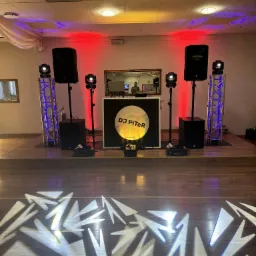 Scena z nagłośnieniem i oświetleniem DJ PiTer na drewnianym parkiecie z efektami świetlnymi. Widoczne kolumny, reflektory i konstrukcja aluminiowa.