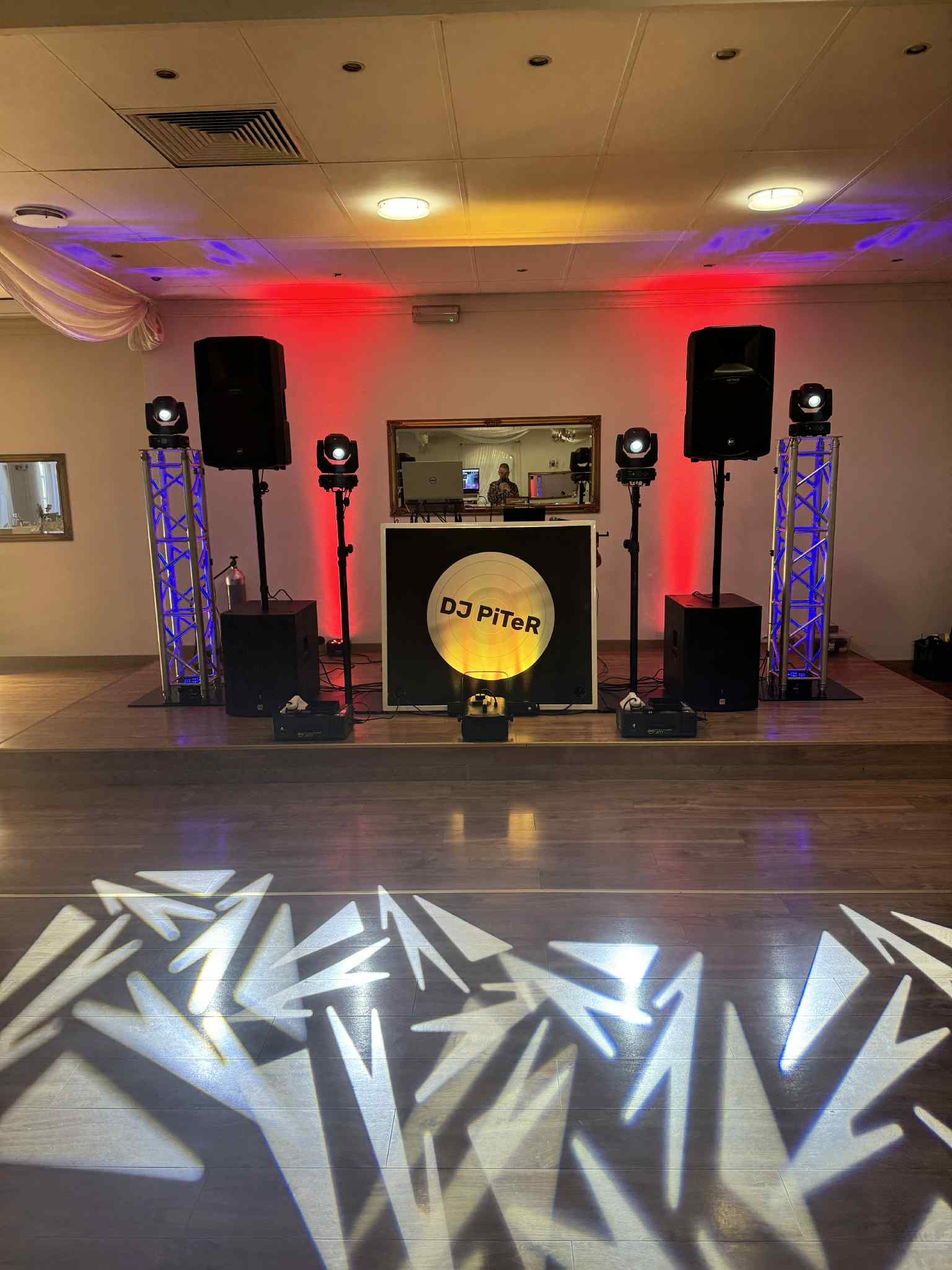 Scena z nagłośnieniem i oświetleniem DJ PiTer na drewnianym parkiecie z efektami świetlnymi. Widoczne kolumny, reflektory i konstrukcja aluminiowa.