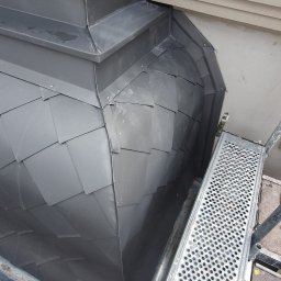 Imperium Dach - Szary, metalowy dach z łupków w kształcie kopuły z detalami architektonicznymi i fragmentem rusztowania, widziany z bliska pod kątem.