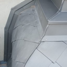 Imperium Dach - Szczegółowe ujęcie obróbki blacharskiej na dachu zabytkowej kamienicy, z widocznymi elementami dekoracyjnymi elewacji i metalowymi płytkami ułożonymi w unikalny wzór.