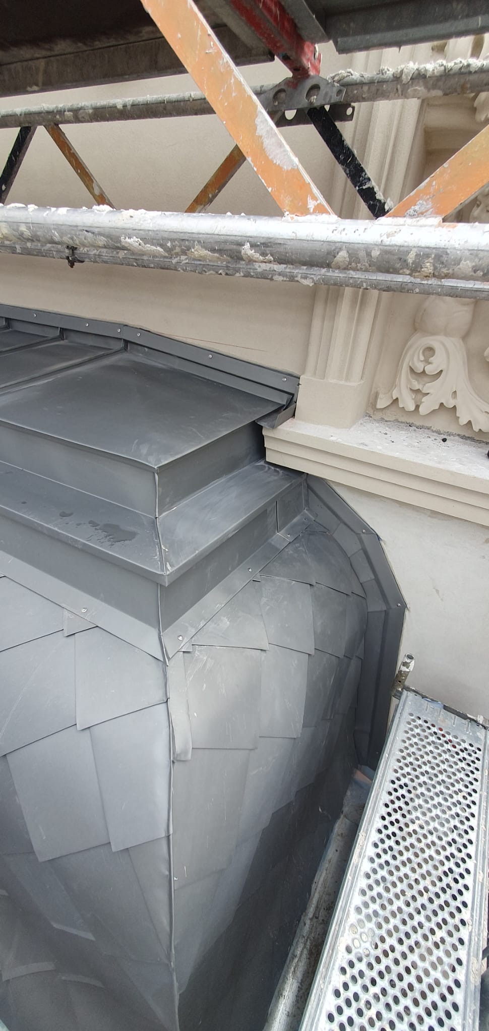 Szary dach z blachy płaskiej na kopule budynku, widok z góry ze rusztowania. Detale architektoniczne i obróbki blacharskie.