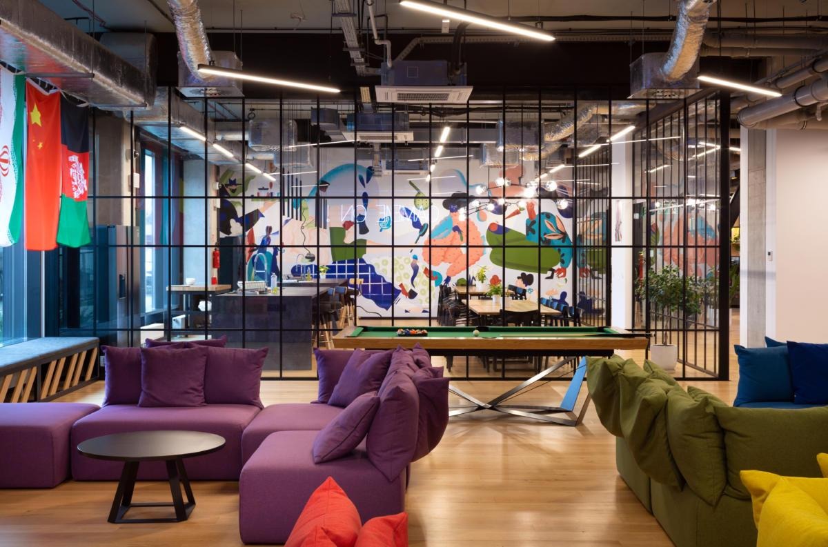 Nowoczesna przestrzeń biurowa z bilardem, kolorowym muralem i flagami, widok z wygodnej sofy.