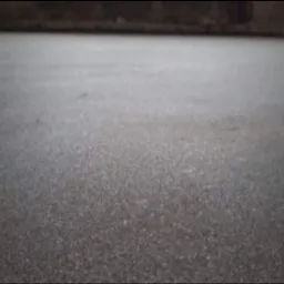 Szara, jednolita posadzka z delikatną fakturą, widoczny fragment metalowej listwy przypodłogowej przy prawej krawędzi.