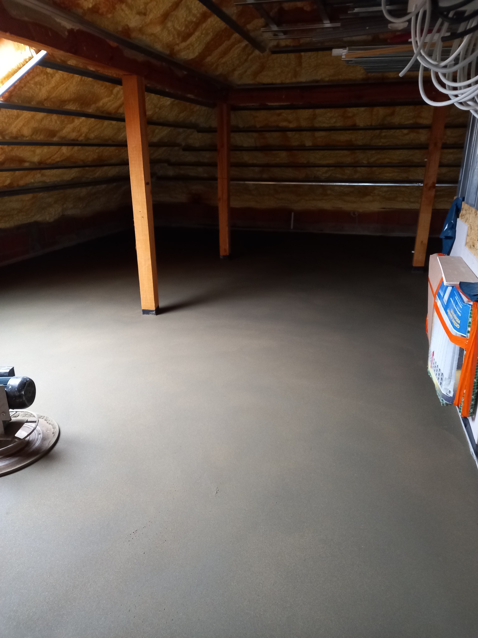 Świeżo wylana, gładka posadzka jastrychowa na poddaszu z widoczną maszyną do zacierania i ociepleniem stropu