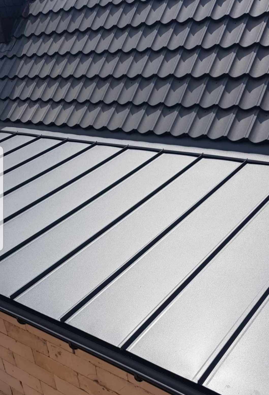 Szary dach z blachy trapezowej z widoczną rynną i fragmentem ściany budynku z cegły