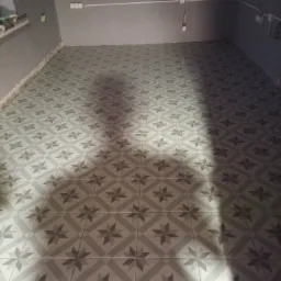 Ułożona szara podłoga z wzorem gwiazdy w nowo wykończonym pomieszczeniu, widoczne szare ściany i wystające przewody elektryczne.