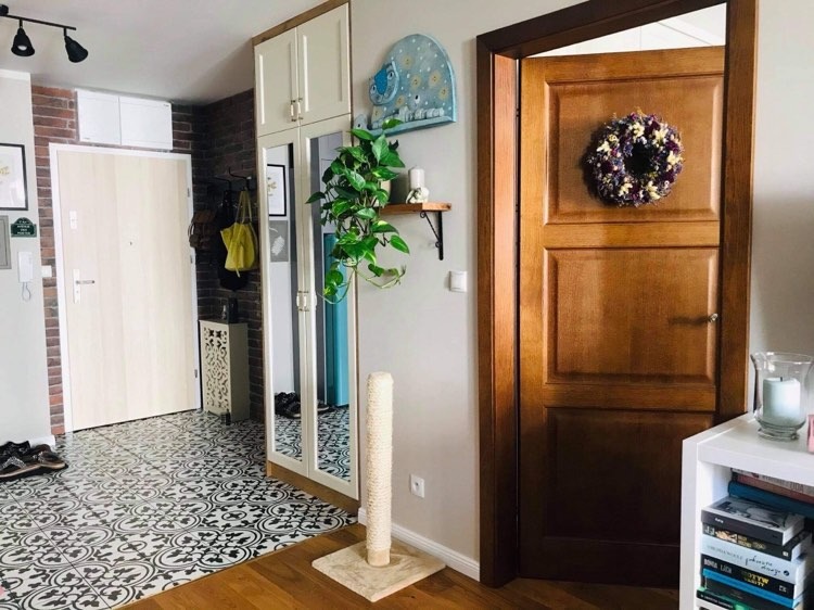 Przedpokój w stylu eklektycznym: białe drzwi wejściowe, wzorzysta podłoga, ceglana ściana, szafa z lustrem, drewniane drzwi wewnętrzne z wieńcem, roślina pnąca w szklanej kuli.