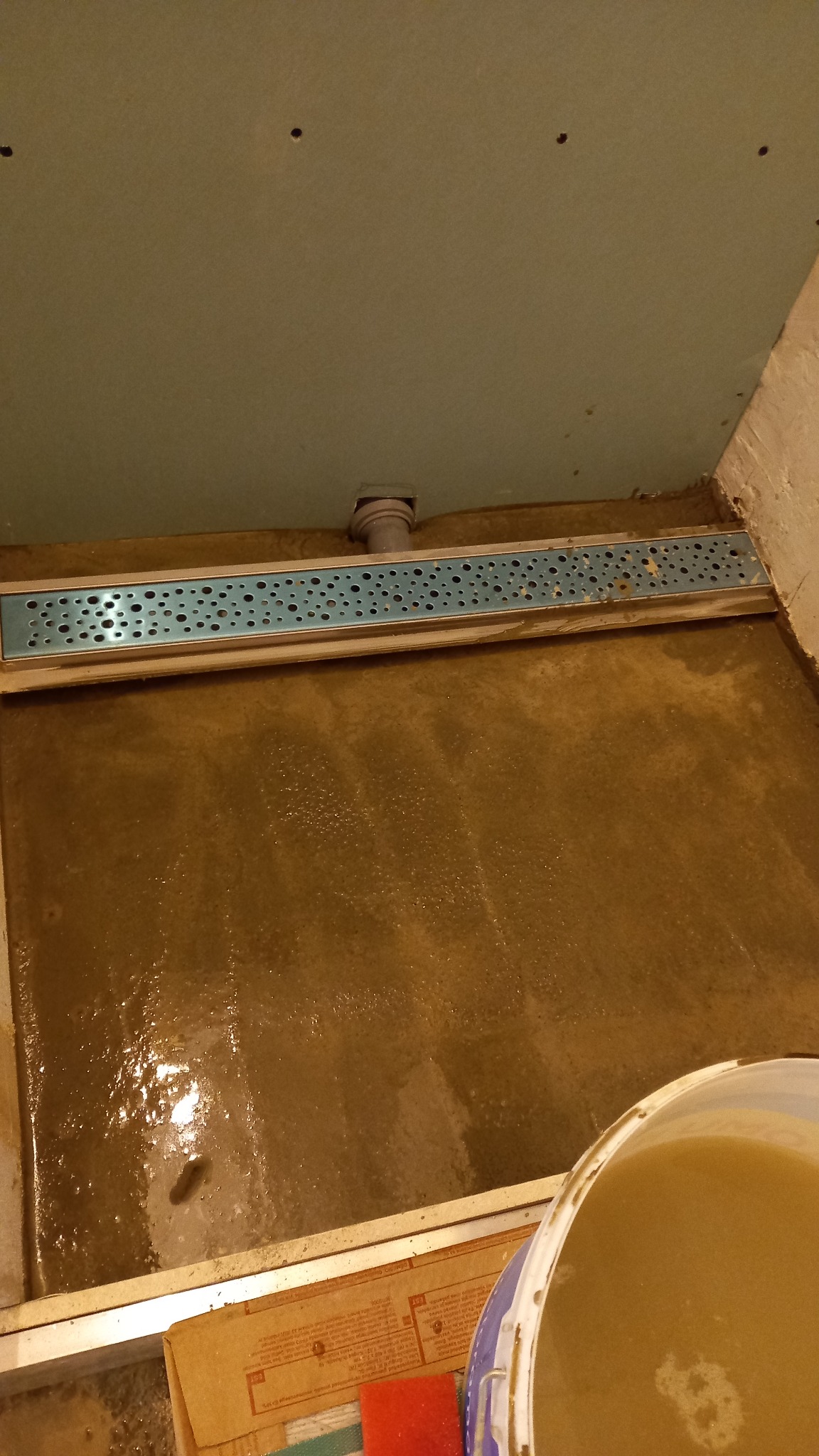 Przygotowanie podłoża pod prysznic: wylewka z odpływem liniowym, ściany z płyt karton gips, widoczny kubeł z zaprawą.