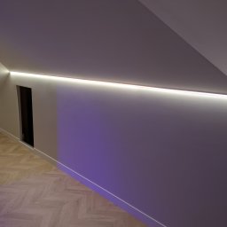 POWERDEK Klaudiusz Kulipczuk - Oświetlenie LED wkomponowane w skos sufitu poddasza, z widocznym wejściem do garderoby i parkietem ułożonym w jodełkę. Nowoczesny design z subtelnym fioletowym podświetleniem ściany.