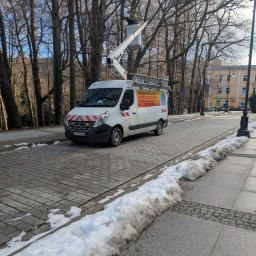 POWERDEK Klaudiusz Kulipczuk - Pracownik w podnośniku koszowym naprawia oświetlenie uliczne. Biały samochód z logo firmy elektrycznej zaparkowany na brukowanej ulicy w zimowy dzień.