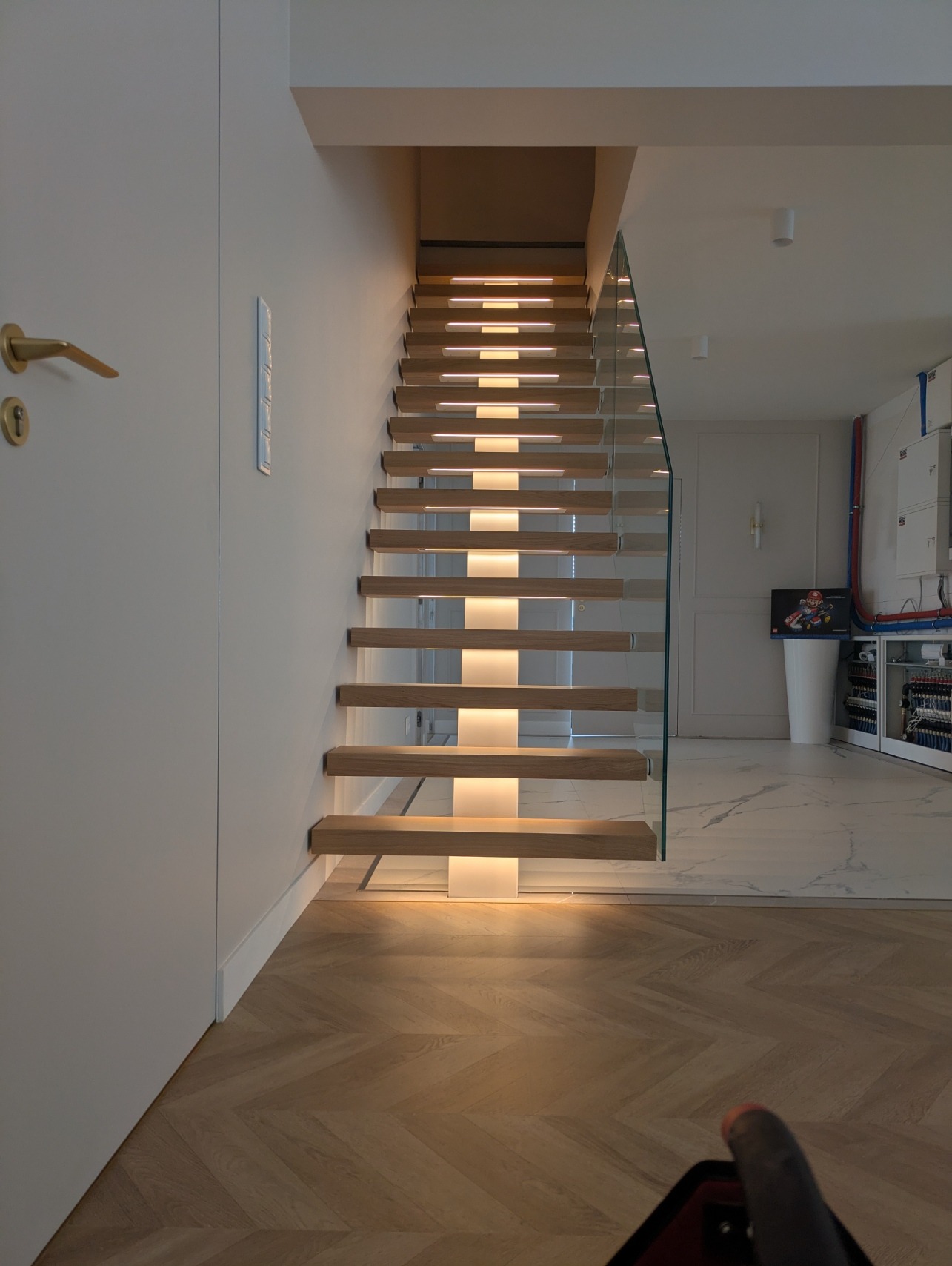 Nowoczesne schody z podświetleniem LED, drewniane stopnie, szklana balustrada. Minimalistyczny design, jasne wnętrze, parkiet w jodełkę.