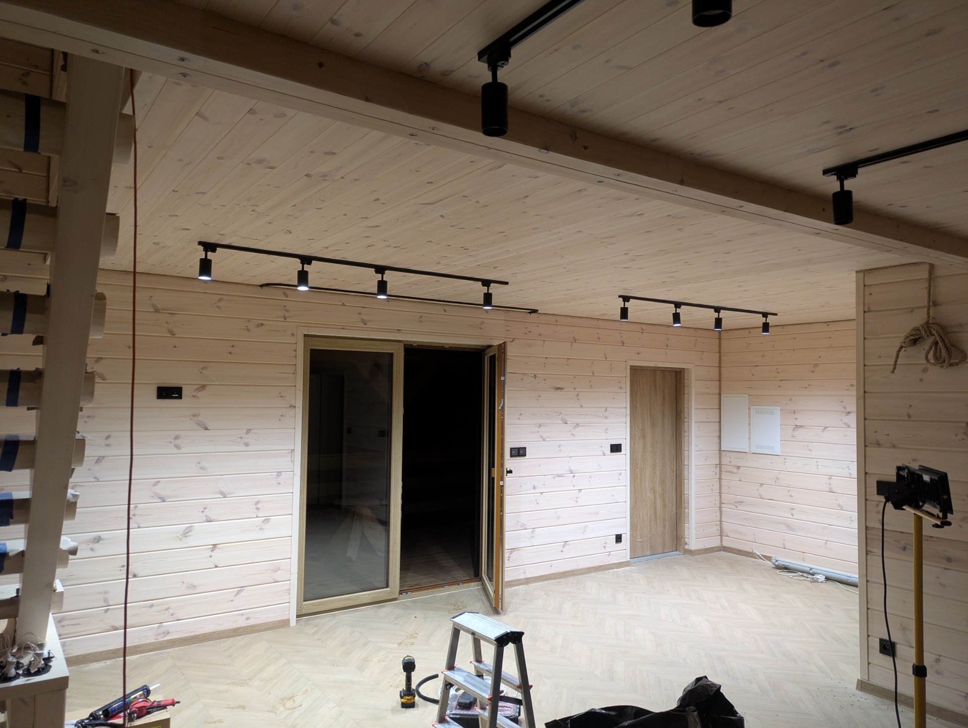 Drewniane wnętrze z zamontowanym systemem szynoprzewodów oświetleniowych z reflektorami punktowymi. Widoczne narzędzia i drabina sugerują trwający montaż.