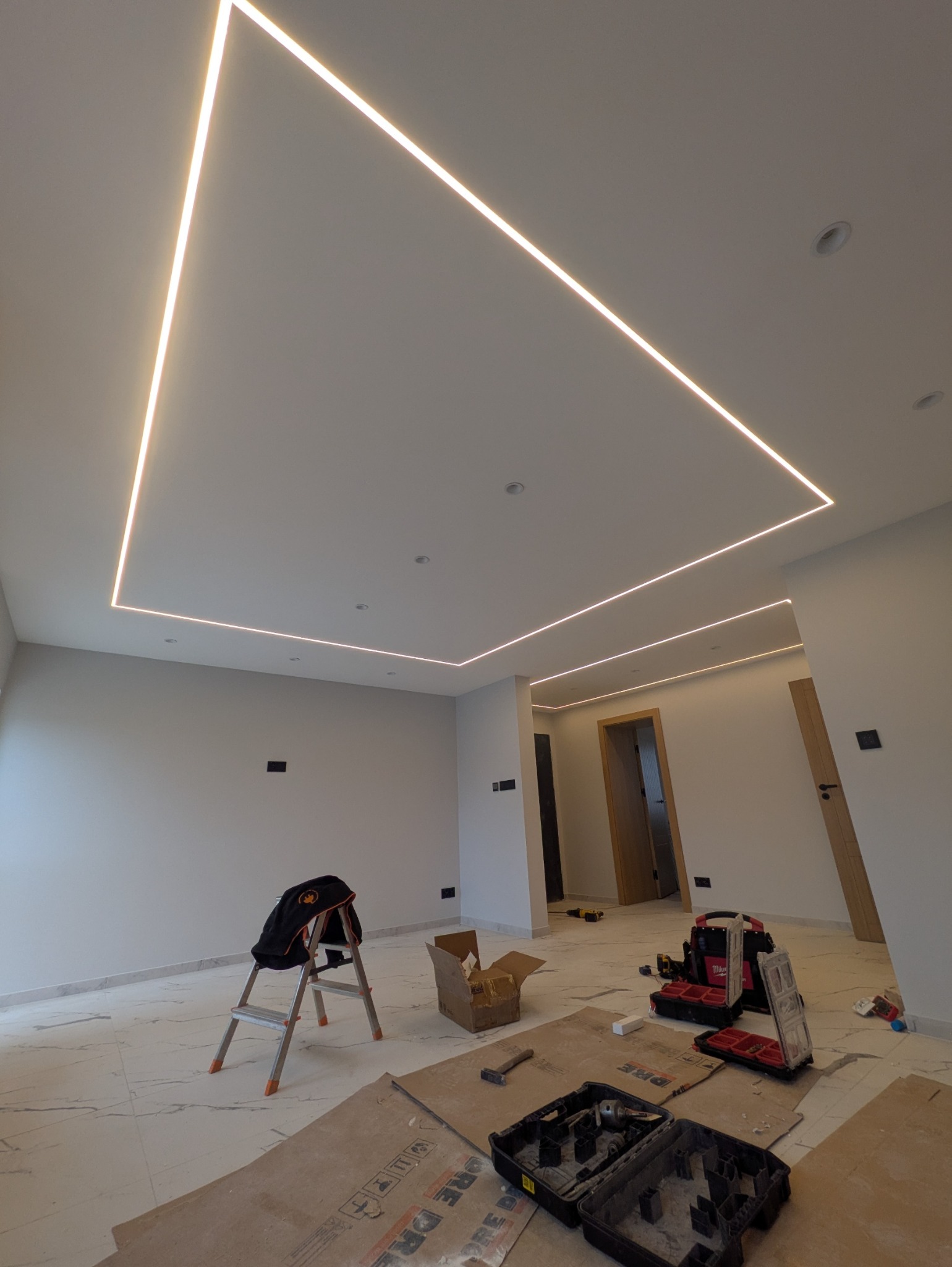 Nowoczesne oświetlenie LED w kształcie kwadratu na suficie, widok z dołu. Na podłodze narzędzia i drabina, co sugeruje prace wykończeniowe.