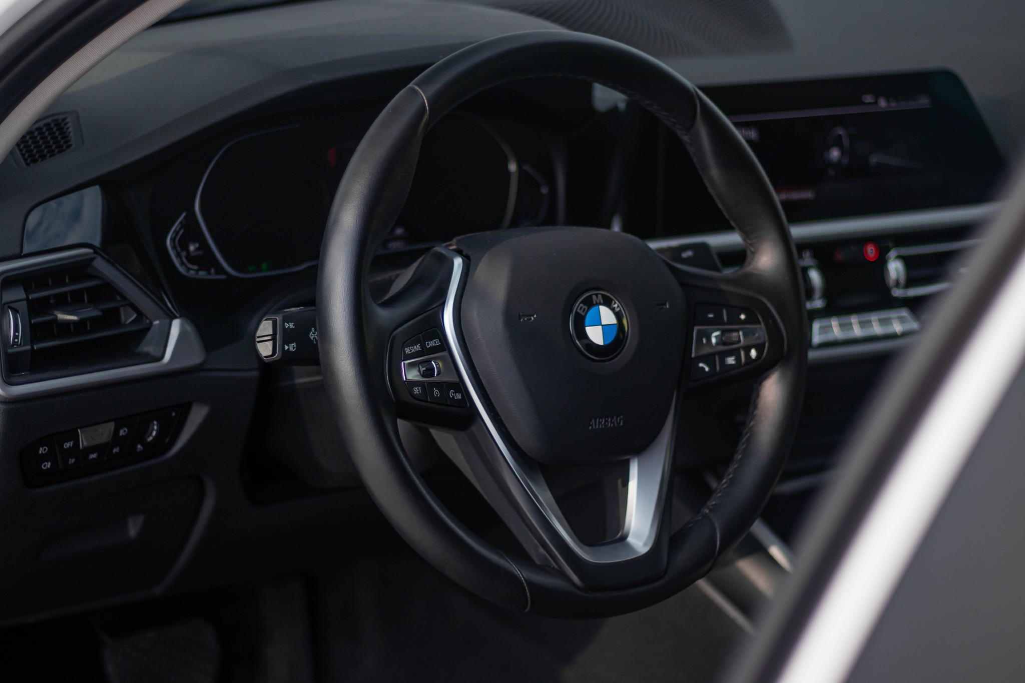 Wnętrze samochodu BMW z czarną skórzaną kierownicą, widoczne logo marki, deska rozdzielcza i elementy sterowania