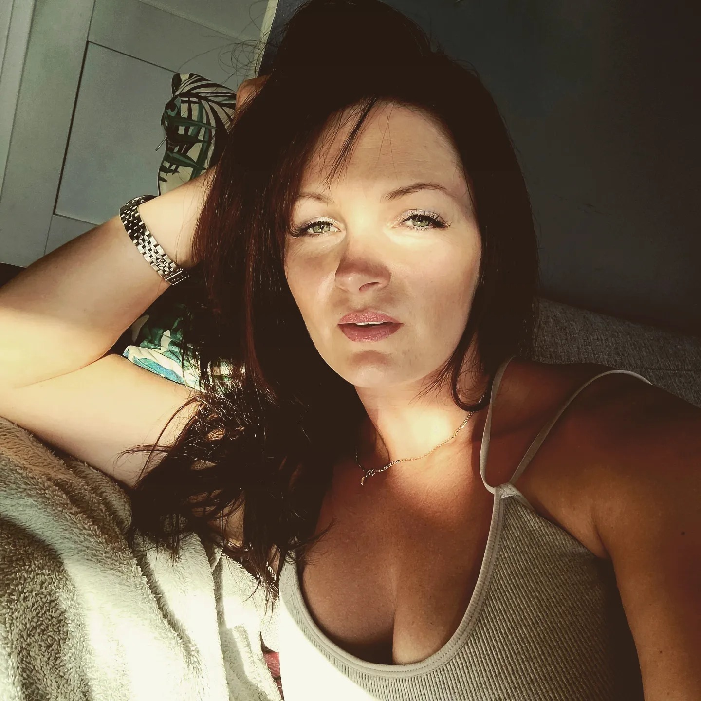 Portret kobiety z brązowymi włosami, srebrnym zegarkiem i delikatnym makijażem w naturalnym świetle.