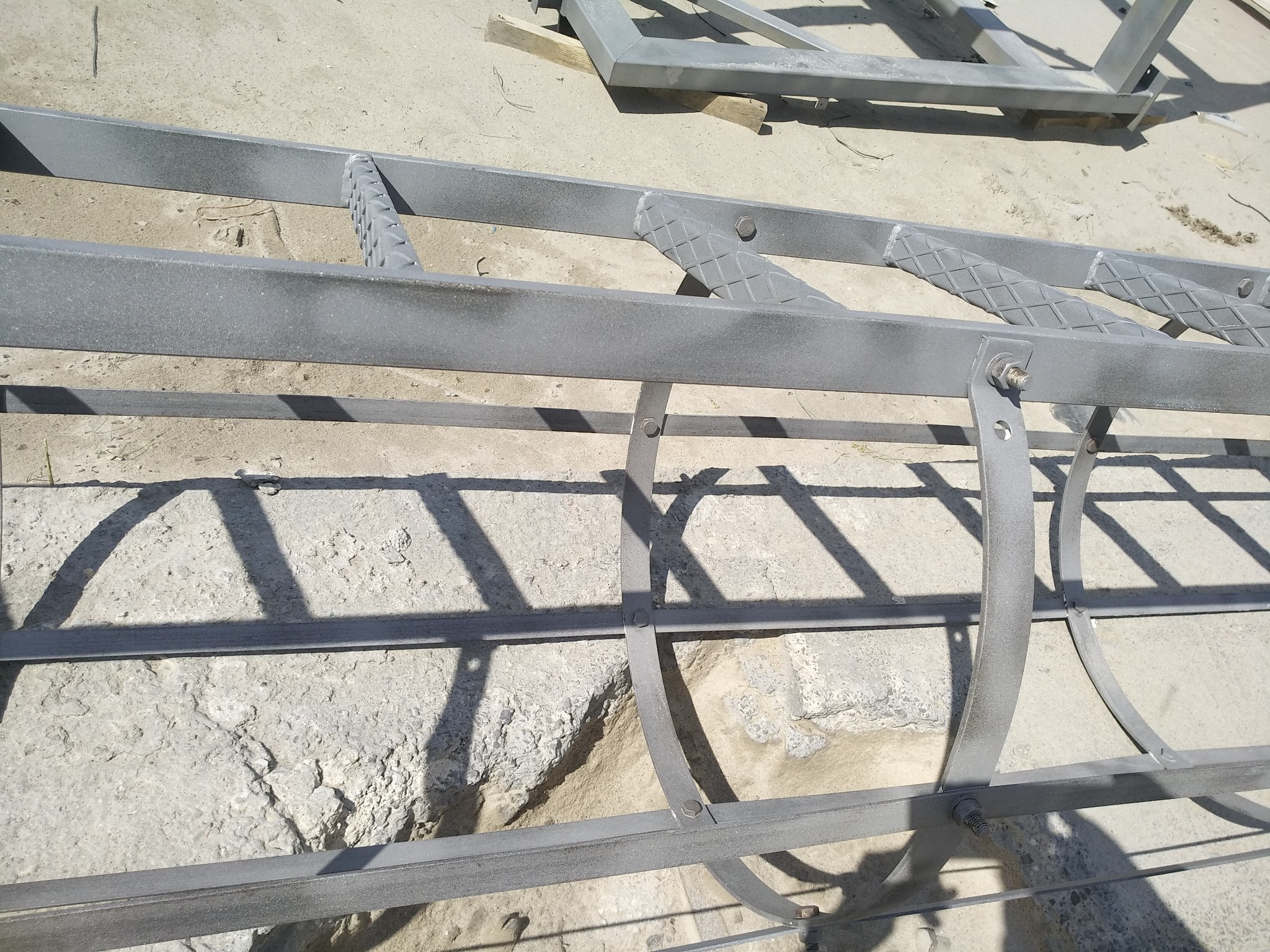 Metalowa konstrukcja pomalowana proszkowo na szaro, leżąca na betonowym podłożu. Widoczne detale łączeń i faktura farby.