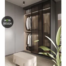 Wnętrze garderoby z przesuwnymi drzwiami z ryflowanego szkła, oświetleniem LED i beżową pufą na drewnianej podłodze, z widocznym logo projektanta.