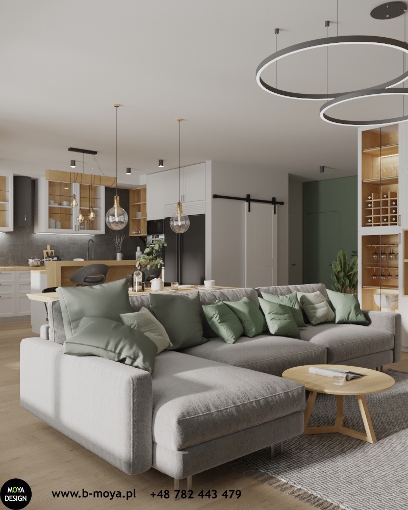 Jasnoszara sofa narożna z zielonymi poduszkami w nowoczesnym salonie z otwartą kuchnią, oświetlonymi okrągłymi lampami sufitowymi i drewnianym stolikiem kawowym.