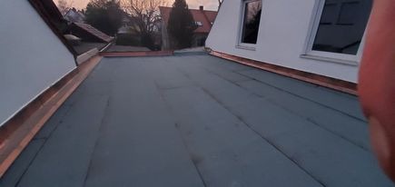 Płaski dach pokryty papą termozgrzewalną z miedzianymi obróbkami blacharskimi, widok z góry na fragment dachu i okna dachowe