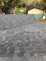 Szary dach pokryty gontem bitumicznym, widok z góry na fragment dachu z ogrodem w tle.