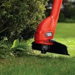 Czerwono-czarna podkaszarka Black&Decker przycinająca trawę przy krzewie, widoczne ostrze i fragment trawnika.