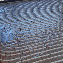 Instalacja ogrzewania podłogowego w Strzelnie: białe rury ułożone na srebrnej folii z czerwoną kratką, widok z góry na przygotowany system przed wylewką.