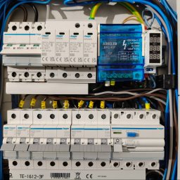 ELWM SPÓŁKA Z OGRANICZONĄ ODPOWIEDZIALNOŚCIĄ - Rozdzielnica elektryczna z zamontowanymi zabezpieczeniami przeciwprzepięciowymi Hager, modułem ADELID BRL 407 i miernikiem napięcia, widoczne kable w kolorach niebieskim, brązowym i żółto-zielonym.