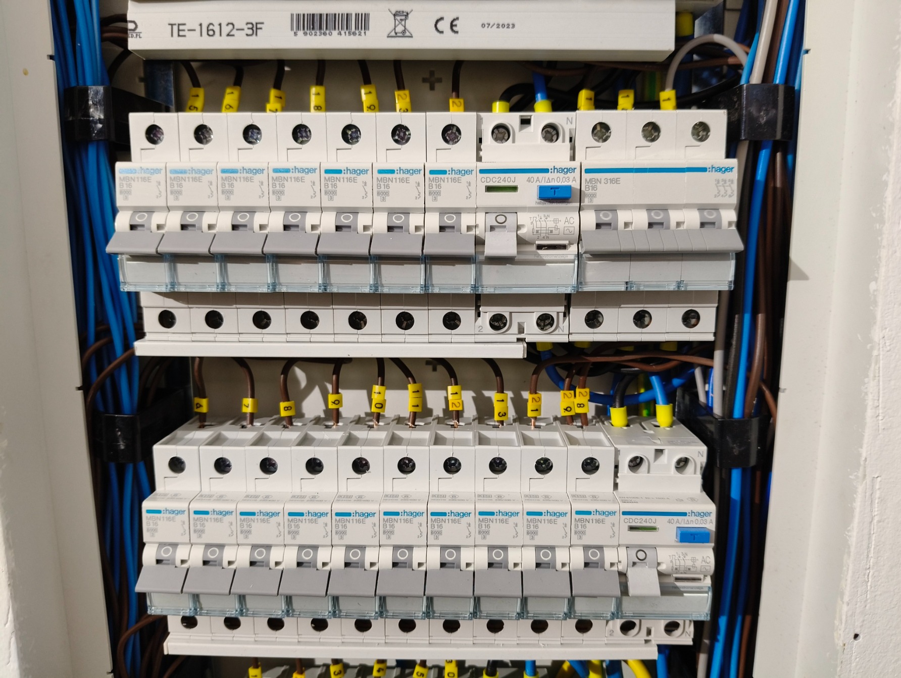 Rozdzielnica elektryczna Hager z zainstalowanymi bezpiecznikami, widoczne przewody o różnych kolorach z numerowanymi oznaczeniami na końcówkach.