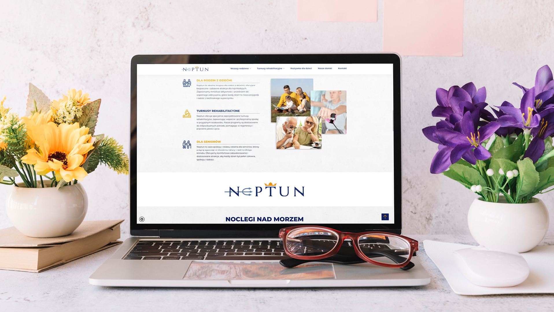 Laptop wyświetlający stronę internetową z ofertą noclegów nad morzem i turnusów rehabilitacyjnych, z okularami na klawiaturze i kwiatami w wazonach po bokach.