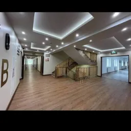 Wnętrze korytarza ośrodka wypoczynkowego z drewnianą podłogą, schodami z drewnianą barierką i nowoczesnym oświetleniem sufitowym.