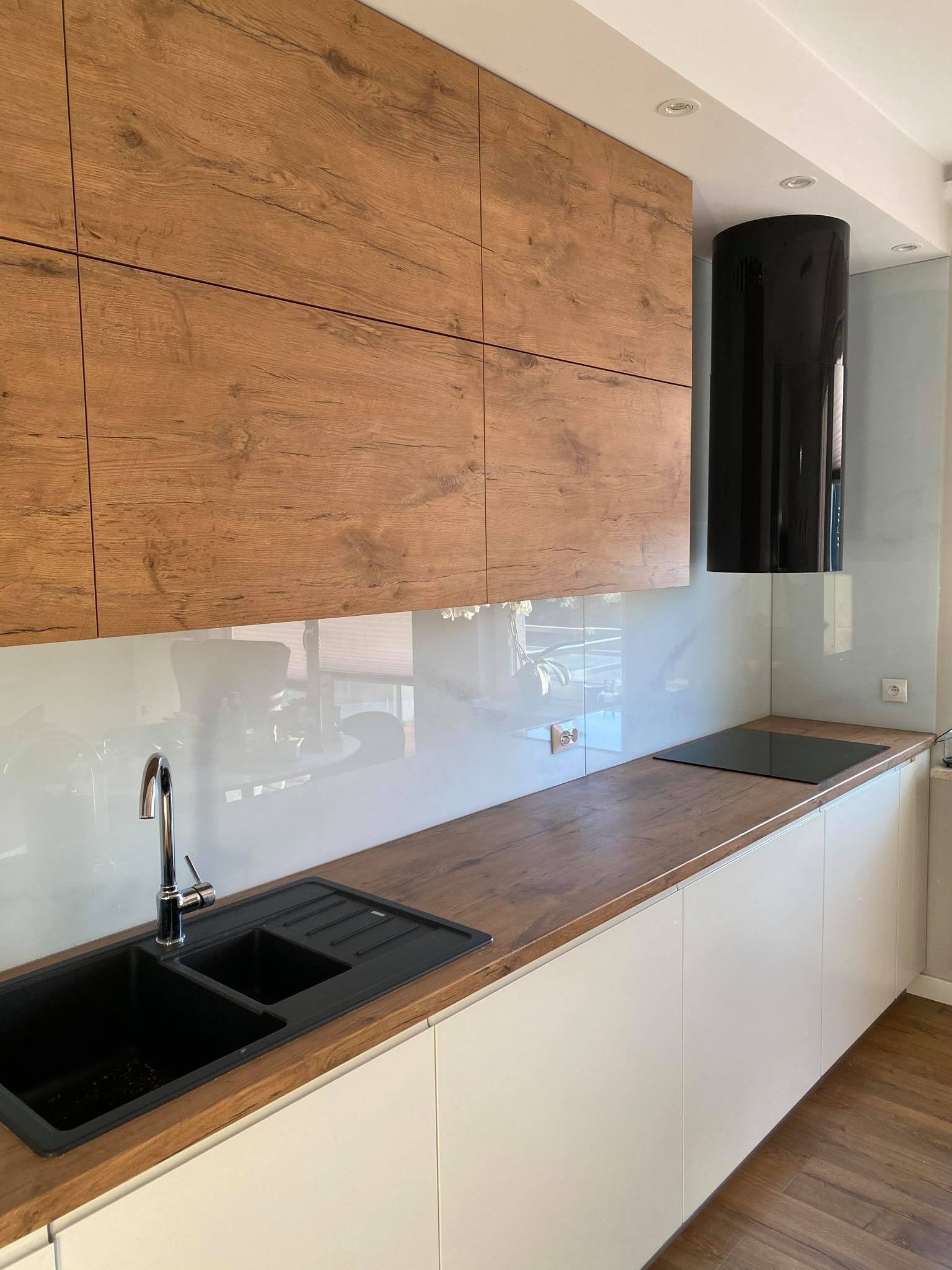 Nowoczesna kuchnia w Gdańsku: drewniane szafki górne z wyraźnym rysunkiem słojów, białe szafki dolne, czarny zlew dwukomorowy i pionowy okap.