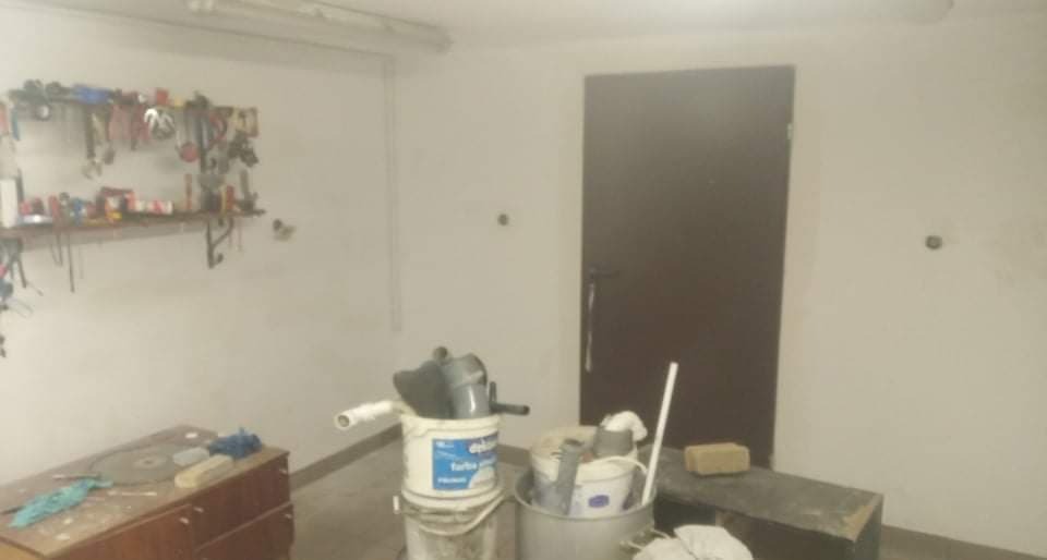 Przygotowania do prac remontowych: pomieszczenie z narzędziami na ścianie, farbami w wiadrach i stolikiem z akcesoriami.