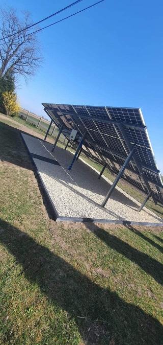 Panel słoneczny na żwirowym podłożu, zamontowany w Bielsku-Białej, widok z dołu ukazujący konstrukcję wsporczą i skrzynkę elektryczną.
