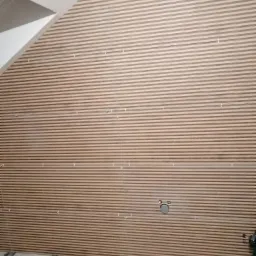 Montaż paneli ściennych z drewnianych listew na poddaszu, widoczne krzyżyki dystansowe i przewody, w tle skośny sufit.