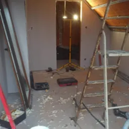 Adaptacja poddasza: widok na wnętrze z zamontowaną konstrukcją metalową pod płyty karton-gips, widoczne narzędzia, drabina i resztki materiałów budowlanych.