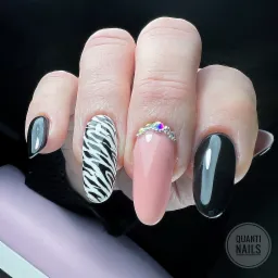 Dłoń z manicure hybrydowym: dwa paznokcie czarne z połyskiem, jeden w zebrę, jeden różowy z ozdobnym pierścieniem z kamieni, na czarnym tle