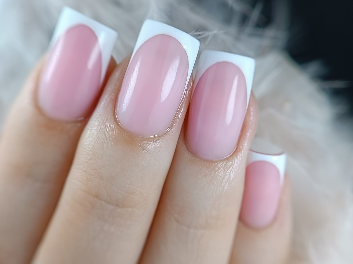 Delikatny, różowy manicure francuski z kwadratowymi końcówkami na tle puszystego, białego materiału.