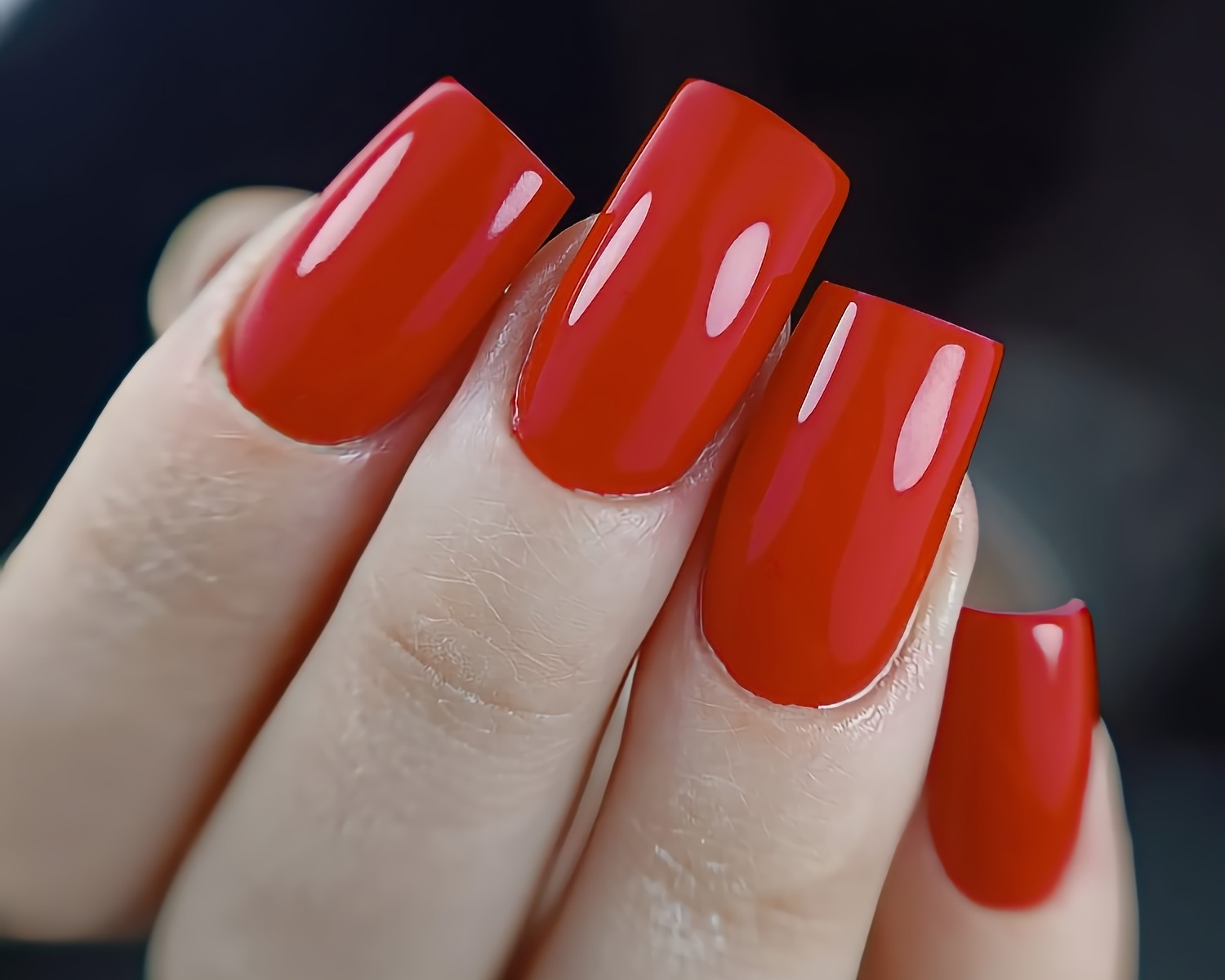 Zbliżenie na dłoń z czerwonym, kwadratowym manicure hybrydowym z wyraźnym połyskiem.