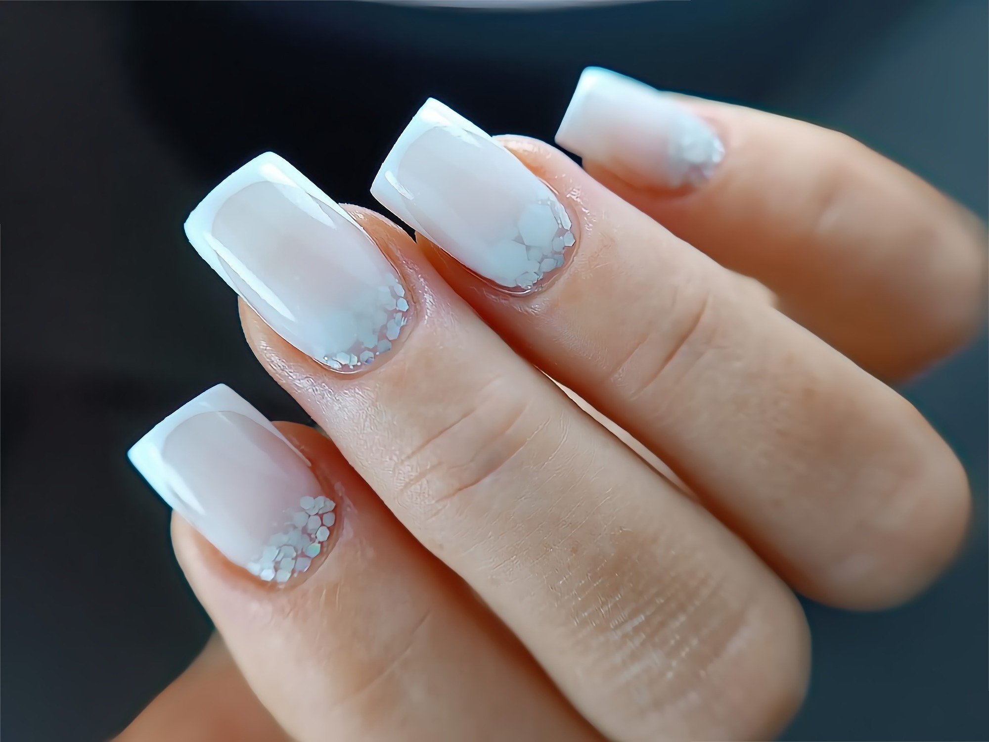 Delikatny manicure hybrydowy z białym french ombre i srebrnymi drobinkami na kwadratowych paznokciach.