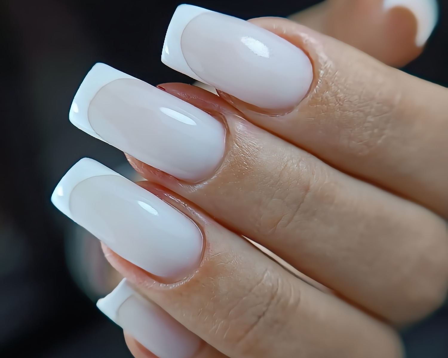 Zbliżenie na dłoń z kwadratowymi paznokciami w stylu french manicure, z wyraźnym, białym wykończeniem i mlecznym odcieniem bazy.