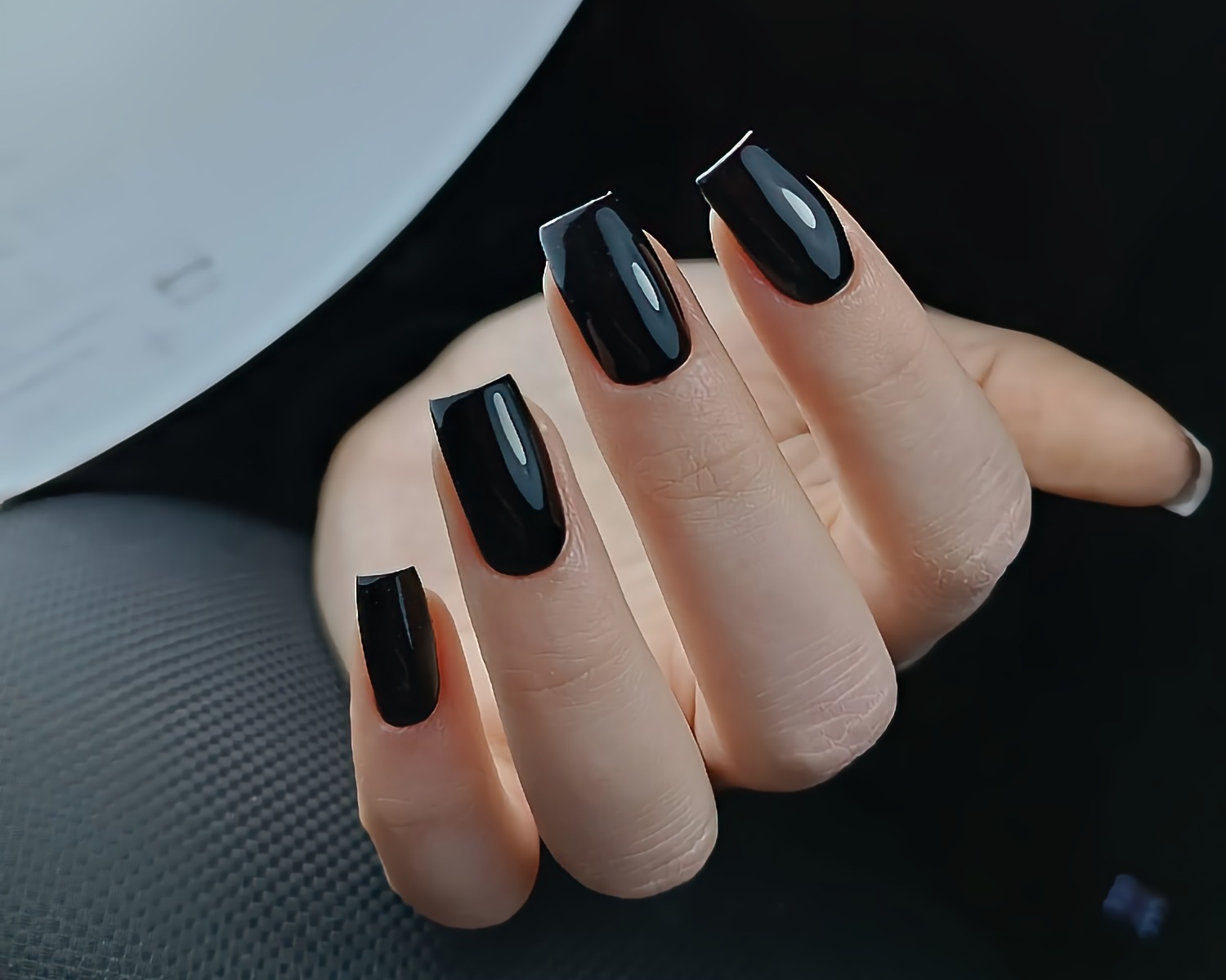 Dłoń z czarnymi, błyszczącymi paznokciami o kwadratowym kształcie, widoczne minimalne odrosty.
