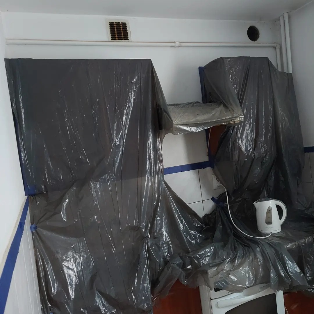 Przygotowanie kuchni do prac wykończeniowych: meble i sprzęty zabezpieczone folią malarską, widoczny czajnik elektryczny na blacie.