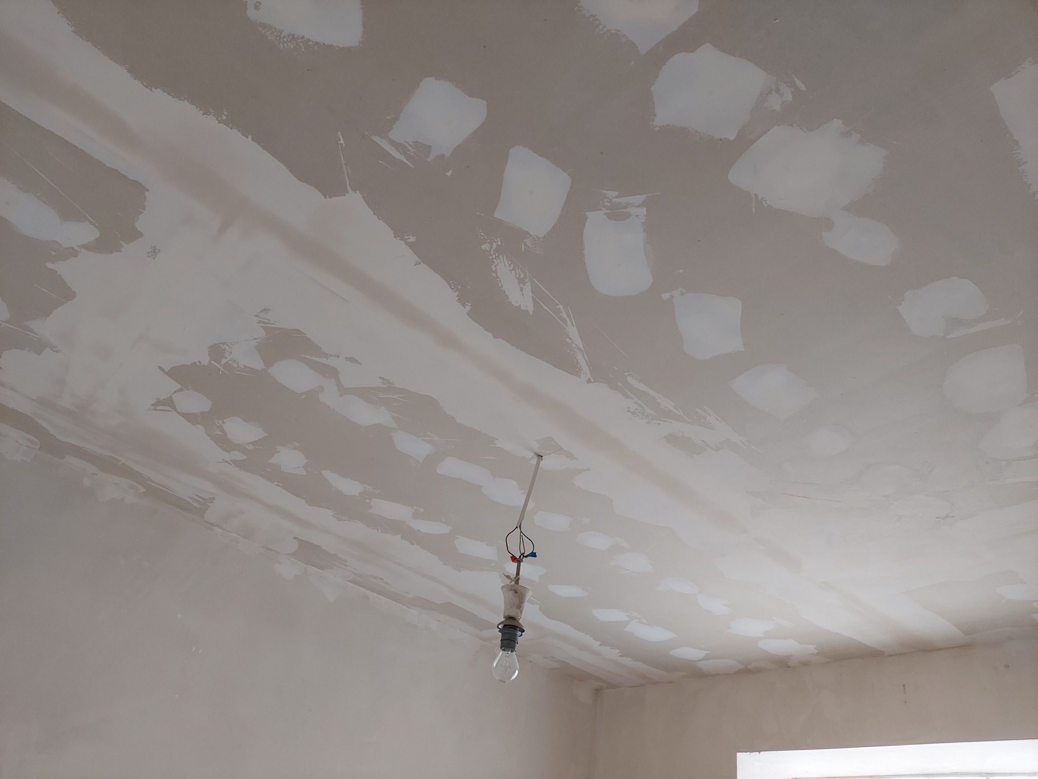 Sufit w trakcie prac wykończeniowych, widoczne nałożone warstwy szpachli i gładzi, surowa żarówka zwisa na kablu.