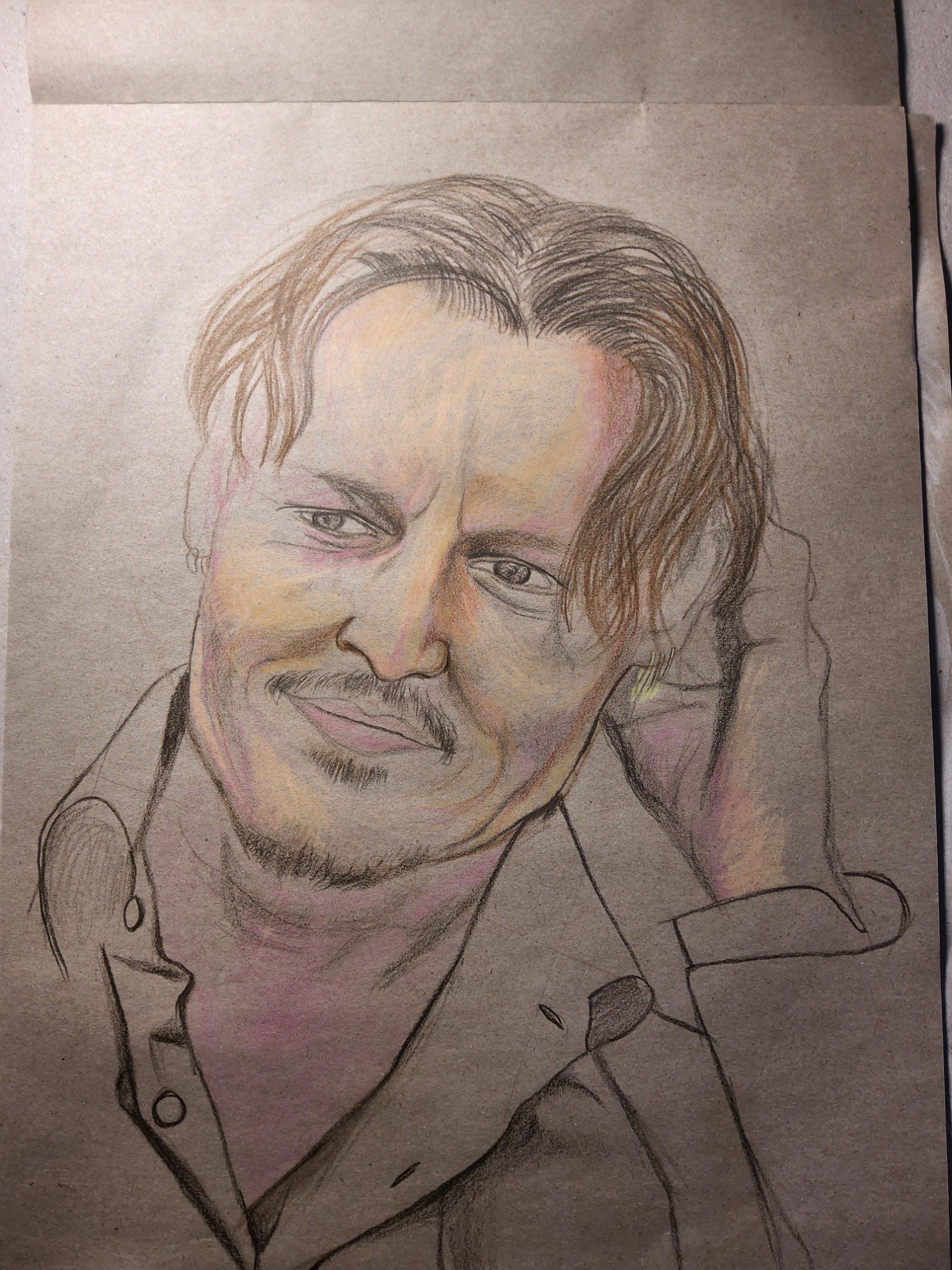 Portret mężczyzny z lekkim uśmiechem, wykonany ołówkiem i kredkami na brązowym papierze, widoczny fragment koszuli i dłoni przy twarzy.