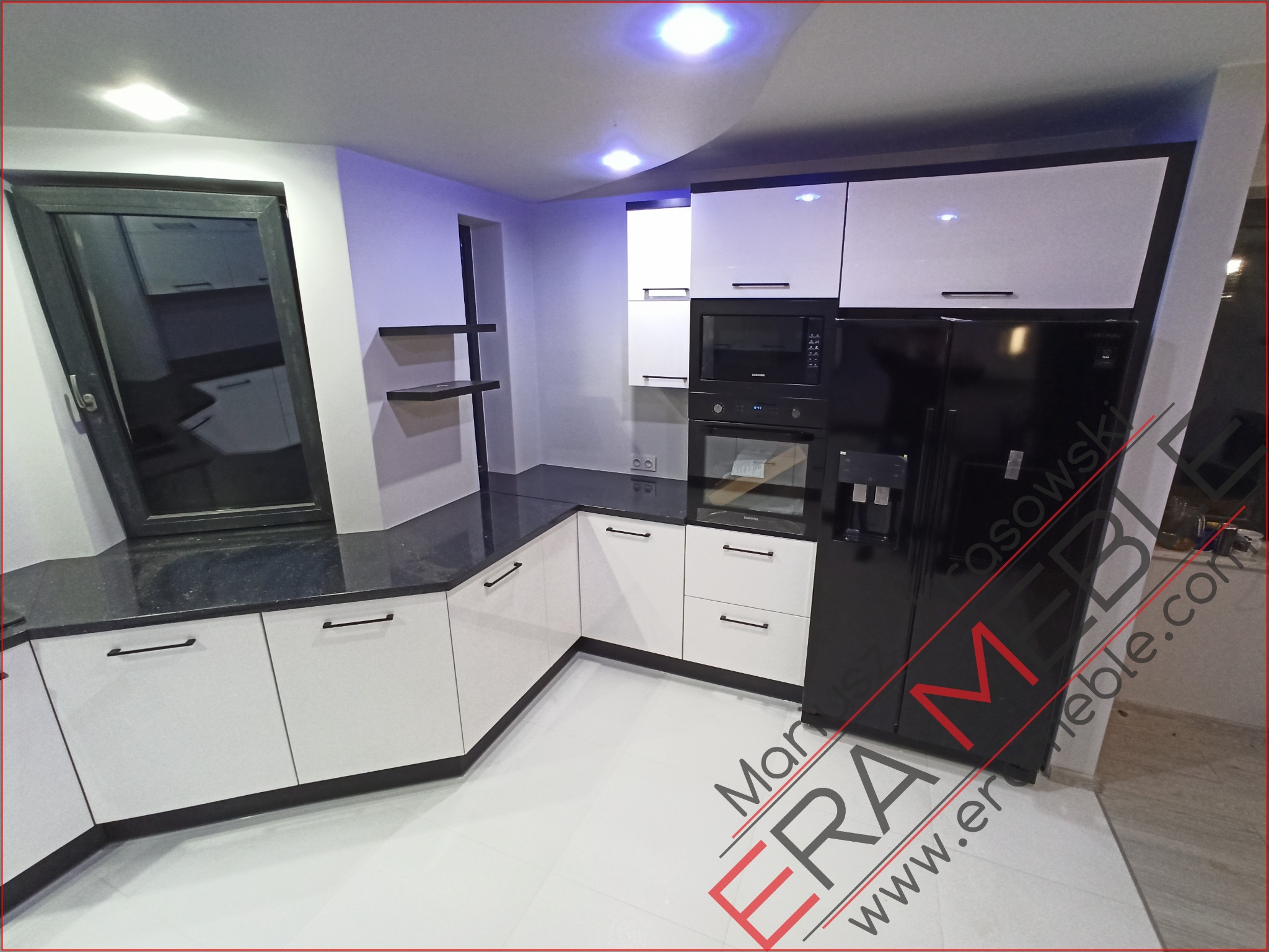 Nowoczesna kuchnia z białymi szafkami i czarnym blatem w Górce, z widoczną czarną lodówką i oświetleniem LED.