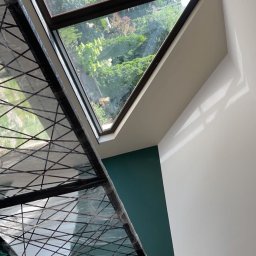 Remonty Budowlane - Montaż okna dachowego w Warszawie, widok z wnętrza na zewnątrz, zabezpieczony stelaż ochronny, ściana pomalowana częściowo na zielono.