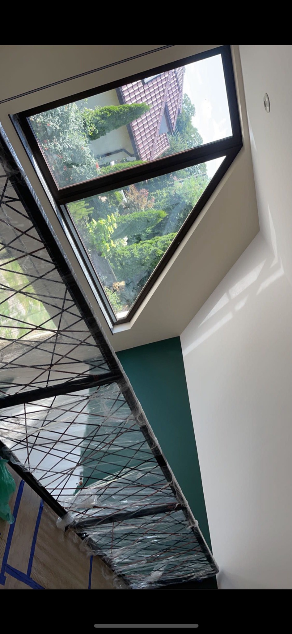Montaż okna dachowego w Warszawie, widok z wnętrza na zewnątrz, zabezpieczony stelaż ochronny, ściana pomalowana częściowo na zielono.