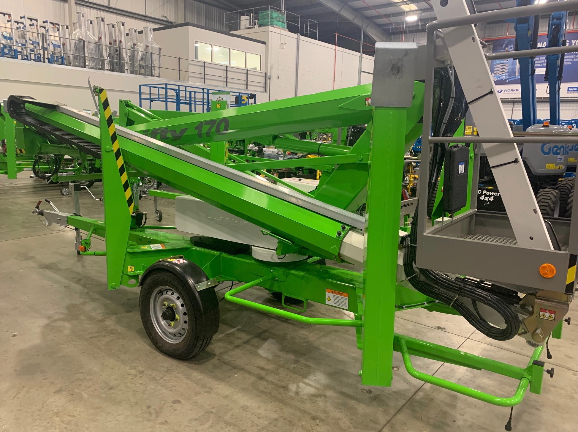 Zielona, przyczepiana platforma podnośnikowa Niftylift 170 z wysięgnikiem teleskopowym, widoczna w hali magazynowej, z widocznymi elementami konstrukcyjnymi i tabliczkami ostrzegawczymi.